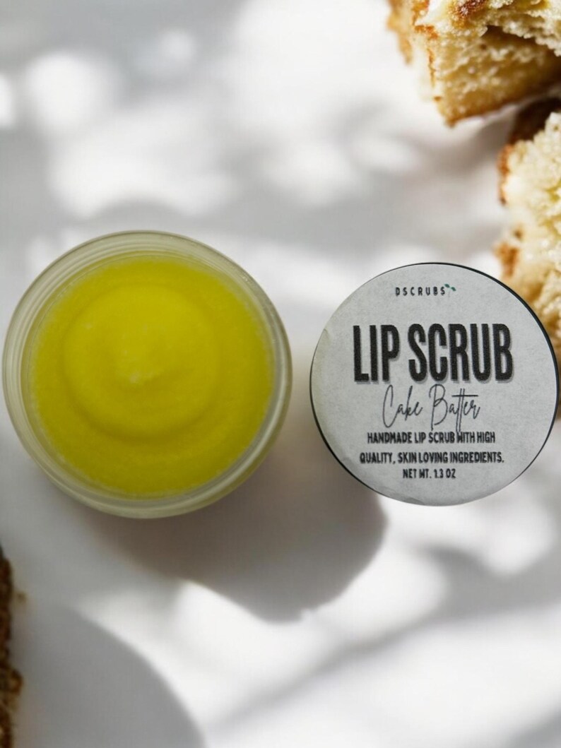 Puede incluir: Un peque&ntilde;o tarro de exfoliante labial amarillo con una etiqueta blanca que dice "DSCRUBS LIP SCRUB Cake Batter HANDMADE LIP SCRUB WITH HIGH QUALITY, SKIN LOVING INGREDIENTS. NET WT. 1.3 OZ"