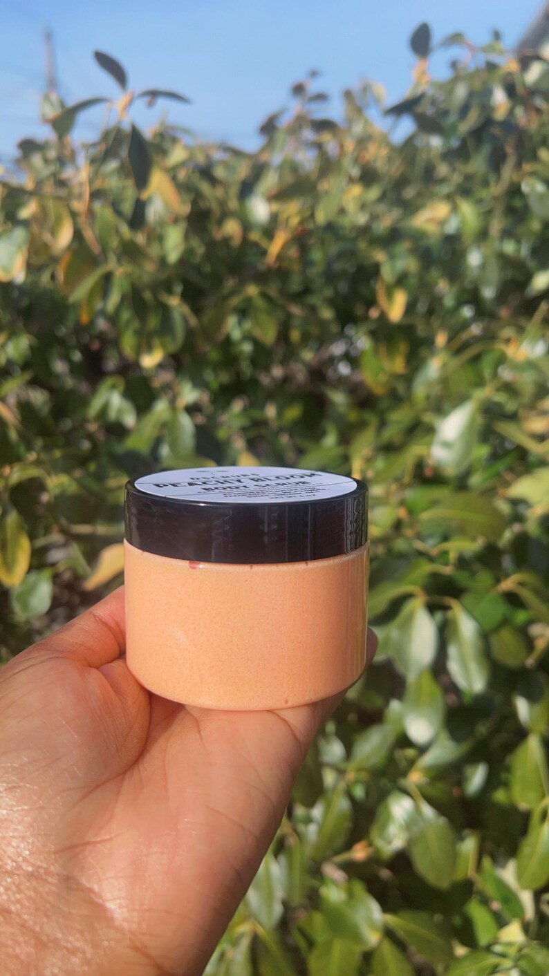 Op de afbeelding: Een lichaams scrub met perzik en bloesem geur in een doorzichtige pot met een zwarte deksel. De pot is gelabeld "Peach Blossom Body Scrub".