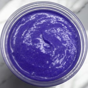 May include: A close-up of a purple hair mask in a clear jar. The mask has a smooth, creamy texture.