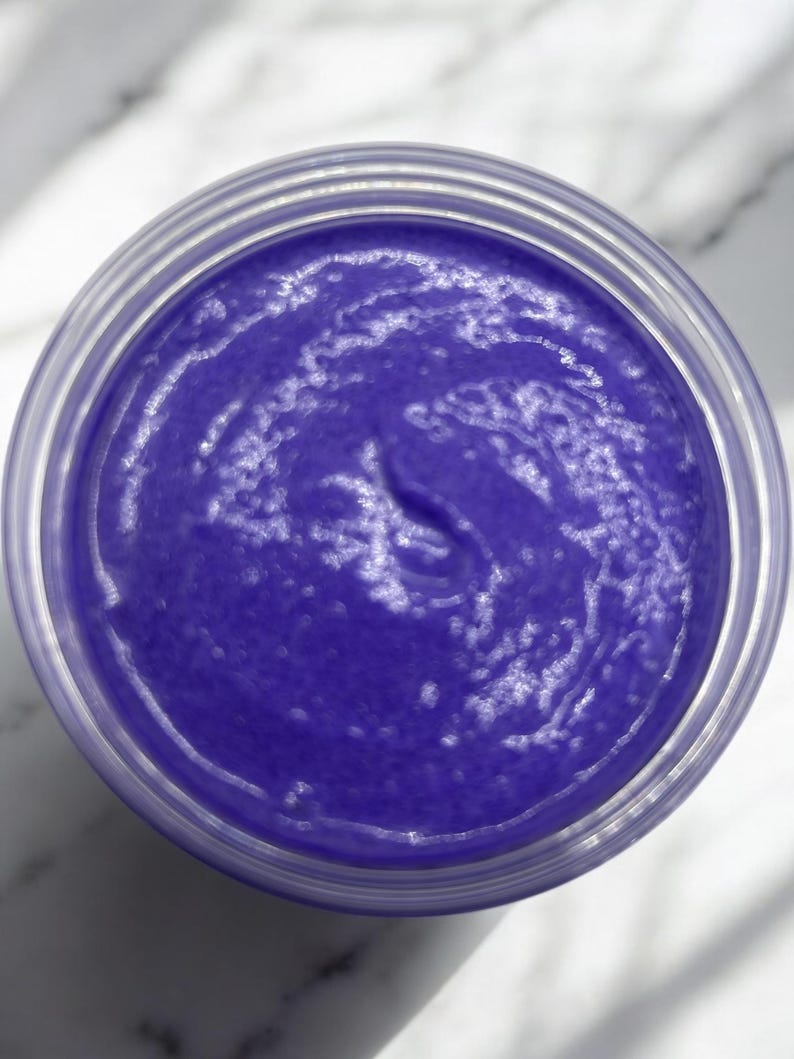 May include: A close-up of a purple hair mask in a clear jar. The mask has a smooth, creamy texture.