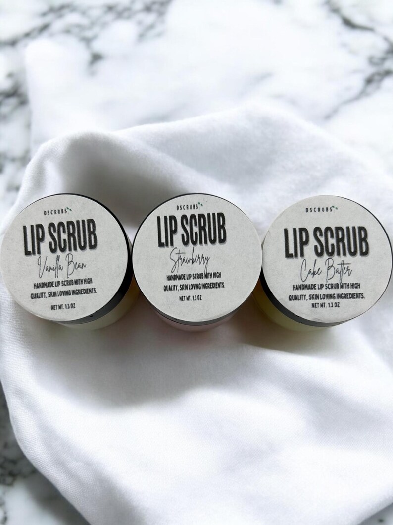 Puede incluir: Tres peque&ntilde;os frascos de exfoliante labial con etiquetas blancas y texto negro. Las etiquetas dicen "Lip Scrub" con los sabores "Vanilla Bean", "Strawberry" y "Cake Batter".