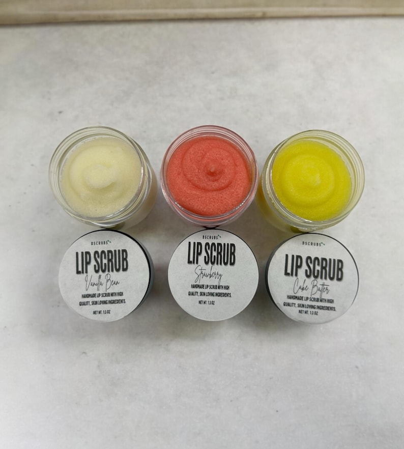 Puede incluir: Tres peque&ntilde;os frascos de vidrio con tapas blancas que contienen exfoliantes labiales. Los frascos est&aacute;n etiquetados con "Lip Scrub" con diferentes sabores: "Vanilla Bean", "Strawberry" y "Cake Batter".