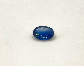 Puede incluir: Una piedra preciosa de zafiro ovalada de color azul intenso con un ligero brillo iridiscente.