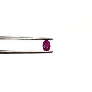 May include: A close-up of a vibrant pink oval-shaped gemstone held by tweezers.