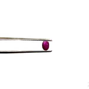 Puede incluir: Primer plano de una gema ovalada de color rosa vibrante sostenida por unas pinzas.