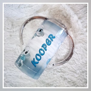 May include: A blue and white personalized sippy cup with a cartoon elephant design and the name "Kooper" printed on it. The cup has two clear plastic handles.
