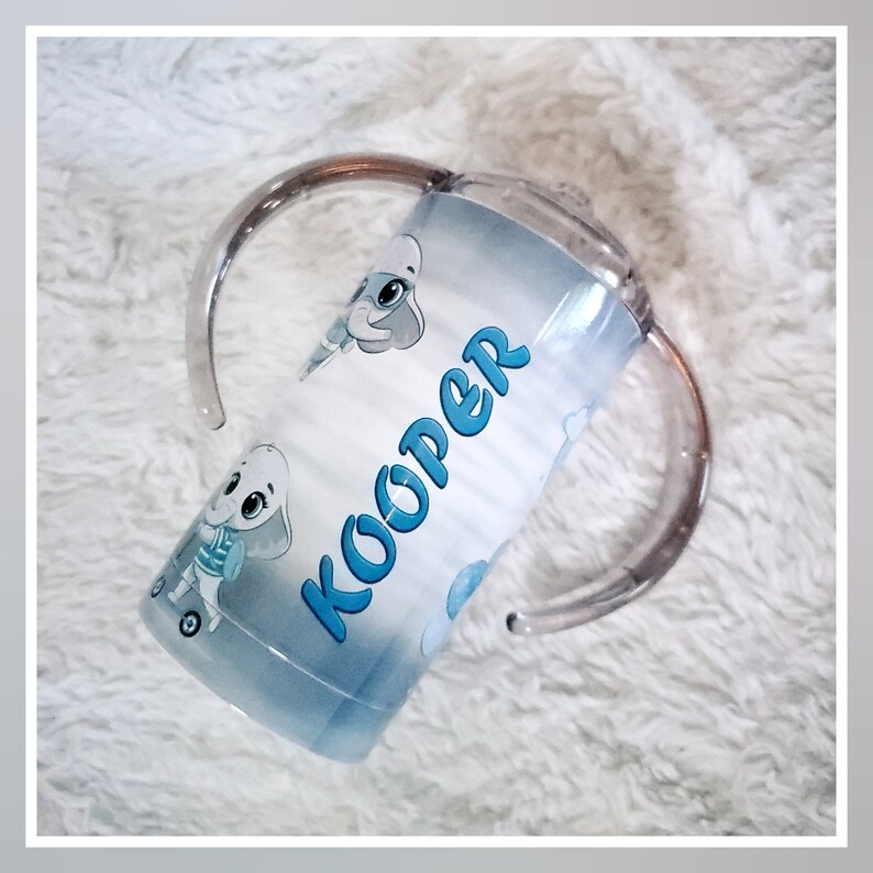 May include: A blue and white personalized sippy cup with a cartoon elephant design and the name "Kooper" printed on it. The cup has two clear plastic handles.