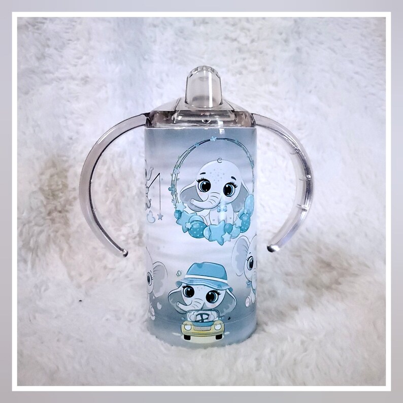 May include: A blue and white stainless steel tumbler with a clear lid and two handles. The tumbler features a design of an elephant with stars and a baby elephant in a car.