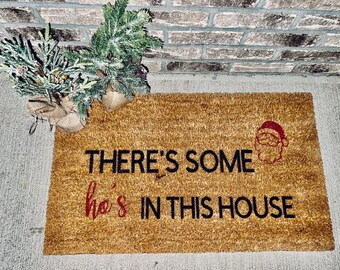 May include: A brown coir doormat with the text "There's some ho's in this house" in black lettering and a red Santa Claus face graphic.