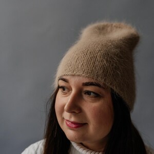 Puede incluir: Una mujer con un gorro de punto marrón claro y peludo y un suéter de punto blanco.
