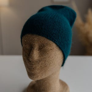 Puede incluir: Un gorro de punto azul turquesa sobre una cabeza de maniquí marrón.