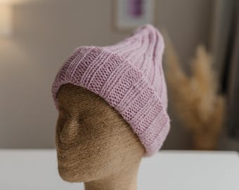 Könnte beinhalten: Eine rosafarbene Strickmütze auf einem braunen Mannequin-Kopf. Die Mütze hat eine gerippte Textur.
