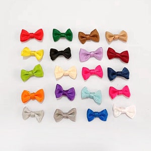 以下が含まれることがあります： 赤、緑、青、黄、紫、ピンク、白など、さまざまな色の小さなサテンリボンボウが20個入ったアソートメント。ボウは白い背景に並べてあります。