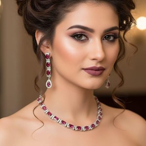 May include: A woman wearing a green strapless dress with gold embroidery, a ruby and diamond necklace, and matching earrings. Her hair is styled in an updo.