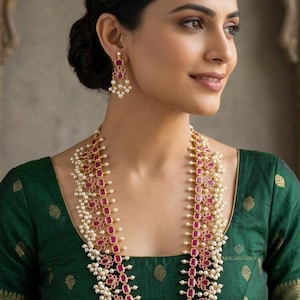 May include: A gold-toned necklace and matching earrings set featuring ruby-colored rectangular stones and small white pearls. The jewelry is worn with a green blouse.