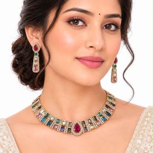 May include: A gold-toned necklace and matching drop earrings set featuring multi-colored rectangular and pear-shaped gemstones. The necklace has a central pear-shaped pink stone surrounded by smaller clear crystals and alternating colored stones.