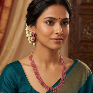 May include: A jewellery set consisting of a necklace and matching drop earrings, both featuring multiple small, faceted, deep pink stones set in a gold-toned metal frame. The necklace has a multi-layered design, and the earrings are floral-shaped.