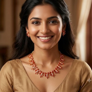 May include: A jewellery set consisting of a necklace and matching earrings, featuring orange, leaf-shaped stones arranged in a floral pattern with small, clear, sparkling accents set in a metallic frame, worn against a plain, light-coloured garment.