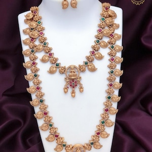 Op de afbeelding: Een goudkleurige sieradenset, inclusief een ketting en oorbellen, tentoongesteld op een witte mannequin. De ketting heeft ingewikkelde ontwerpen met rode en groene accenten. De tekst "JA 355" en "Matte Finish Combo" zijn zichtbaar.