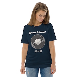 May include: Navy blue t-shirt with a vinyl record graphic. The text on the shirt reads "Groove is in the heart" and "Deee-Lite". The graphic is a black record with white and grey details. The shirt is made of a soft material.