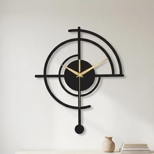 May include: A black wall clock featuring a geometric design with concentric circular arcs and a central solid circle. The clock has thin gold-colored hour and minute hands and a long vertical pendulum arm extending downward with a circular weight at the end.