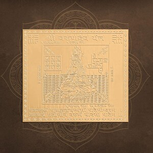 Puede incluir: Un artefacto religioso cuadrado de color dorado con intrincados detalles grabados. La figura central es una deidad sentada con un halo, rodeada de patrones geométricos y texto. El fondo es marrón oscuro con un diseño de mandala decorativo.