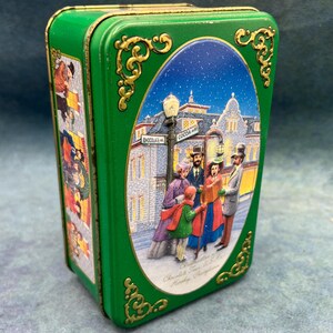May include: A green rectangular tin with a decorative oval image of a winter scene with people and buildings. The tin has gold filigree accents and the words "Chocolate Town U.S.A. Hershey, Pennsylvania."