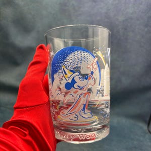 May include: A clear glass with a blue and white design featuring Mickey Mouse in a sorcerer's hat. The design also includes the Epcot ball and fireworks. The glass has the text "Disney World" at the bottom.