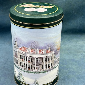 May include: A cylindrical green tin with a lid featuring the Reese's logo. The body of the tin displays a winter scene of High Point Mansion in Hershey, Pennsylvania. The tin is trimmed with gold and black.
