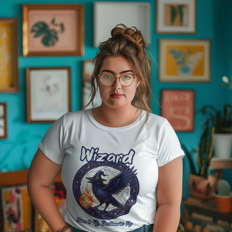 May include: A white t-shirt with a graphic of a black raven wearing a witch's hat and a pentagram. The text "Wizard" is above the raven and "Born to Fly, Destined to Fly" is below the raven.