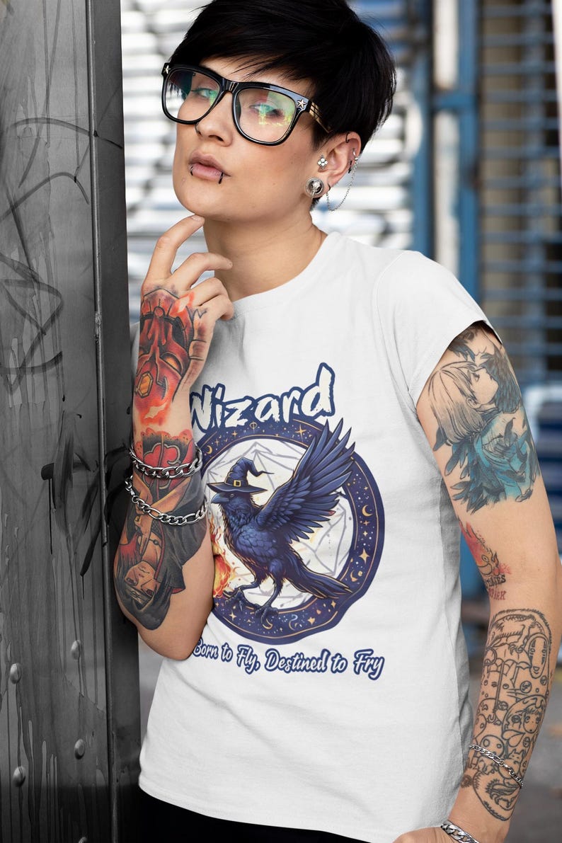 May include: White t-shirt with a blue and white graphic of a raven wearing a witch's hat. The graphic is surrounded by a circle of stars and a pentagram. The text "Wizard" is above the graphic and "Born to Fly. Destined to Fry" is below the graphic.