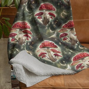 May include: A plush throw blanket with a dark green background featuring a repeating pattern of red and white mushrooms with gold accents. The mushrooms are surrounded by a starry night sky with a subtle glow.