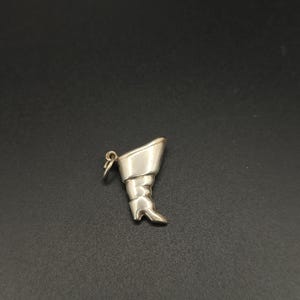 Può includere: Un ciondolo a forma di stivale color argento, con un piccolo anello per attaccarlo a un braccialetto o a una collana. Lo stivale presenta un design dettagliato, tra cui un tacco e pieghe nel materiale. Il ciondolo è probabilmente in metallo.