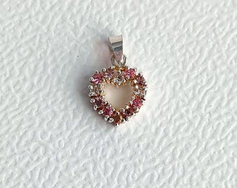 Peut inclure: Un pendentif en argent en forme de cœur avec des strass roses et transparents autour du bord.