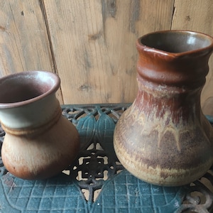 Könnte beinhalten: Zwei braune Keramikvasen mit einem marmorierten Überzug. Die kleinere Vase hat einen weißen Streifen um die Oberseite. Die größere Vase hat eine breitere Öffnung und eine abgerundete Form.