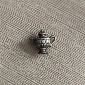 May include: A silver teapot charm with a detailed design. The teapot has a rounded body with a lid and a spout. The charm is small and delicate.