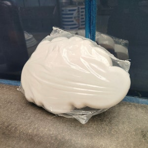 May include: A white cloud-shaped object wrapped in clear plastic. The object is sitting on a grey surface.