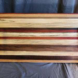 May include: A rectangular serving tray made of various types of wood, with a striped pattern. The tray has two black metal handles on the sides.