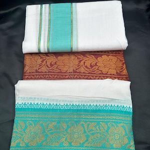 Op de afbeelding: Drie gevouwen witte katoenen sari's met turquoise en gouden bies. De bovenste sari heeft een enkele turquoise streep met gouden accenten. De middelste sari heeft een donkerrode achtergrond met gouden bloemmotieven. De onderste sari heeft een turquoise rand met gouden bloemmotieven.