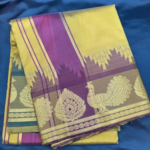 Puede incluir: Un sari de seda amarillo y morado con un diseño de pavo real. El sari tiene un borde dorado y un patrón de rayas moradas y amarillas.