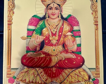 May include: A gold-toned image of a Hindu goddess sitting on a throne with a golden halo. She is wearing a red and green sari, a crown, and jewelry. She is holding a spoon in one hand and a pot in the other. There are offerings of food and fruit in front of her.