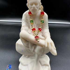 Può includere: Statua in marmo bianco di una figura seduta che indossa una collana di perline rosse e verdi con accenti dorati.