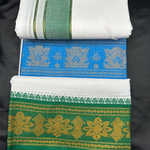 Op de afbeelding: Drie witte katoenen saris met groene en gouden randen. De bovenste sari heeft een groene rand met een gouden streep. De middelste sari heeft een blauwe rand met gouden en zilveren ontwerpen. De onderste sari heeft een groene rand met gouden bloemmotieven.