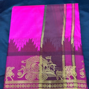 Op de afbeelding: Een roze en paarse zijden sari met een gouden rand en ingewikkelde geweven ontwerpen. De sari heeft een wagen met paarden en een decoratief zigzagpatroon.