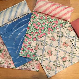 May include: Five different fabric pillowcases with floral and geometric patterns. The pillowcases are folded and arranged on a wooden surface.