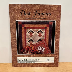 May include: A book cover for a quilting pattern book titled "Past Fancies" by Lynette Jensen & Marilyn Glu. The cover features a quilt with a red, white, and blue color scheme, a basket of flowers, and a brown background with a floral pattern.