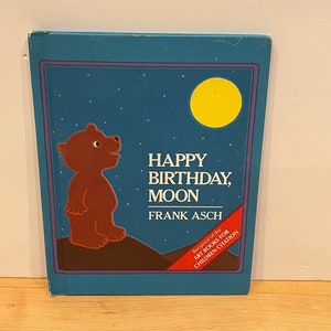 May include: A blue book cover with a brown bear looking up at a yellow moon. The title is "Happy Birthday, Moon" by Frank Asch. The book is a recipient of the "Art Books for Children Citation."