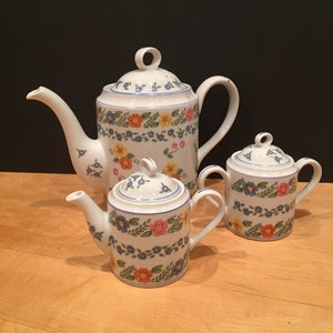 May include: A white porcelain tea set with a floral pattern in shades of blue, yellow, pink, and orange. The set includes a teapot, creamer, and sugar bowl.