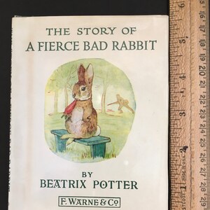 May include: A vintage children's book cover featuring a brown rabbit sitting on a wooden bench with a red carrot in its mouth. The book title is "The Story of a Fierce Bad Rabbit" by Beatrix Potter and published by F. Warne & Co.