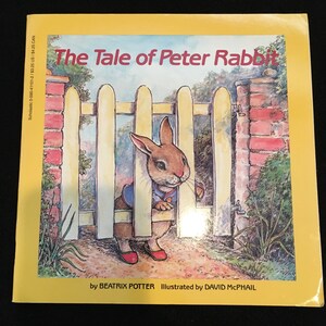 May include: A yellow book cover with the title "The Tale of Peter Rabbit" in red text. The cover features an illustration of Peter Rabbit peeking through a wooden fence. The book is by Beatrix Potter and illustrated by David McPhail.
